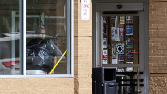 Policajt sa pozerá cez okno v obchode, v ktorom sa strieľalo.
