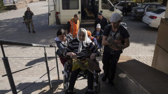 ľudia pomáhajú hendikepovanej žene na Ukrajine