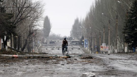Snímka zobrazuje civilistu na bicykli ako prechádza po zničenej ceste v meste Vuhleirsk