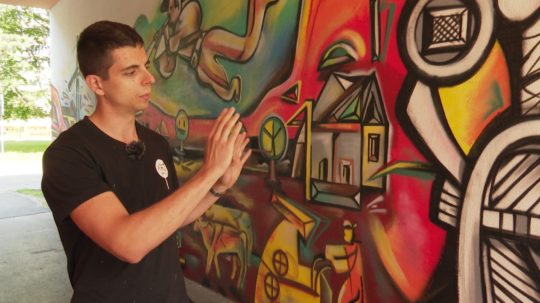 Denis Valašek rozpráva o svojej maľbe na žilinskom sídlisku, pri ktorej stojí.