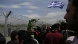 Migranti držia grécku zástavu pri plote