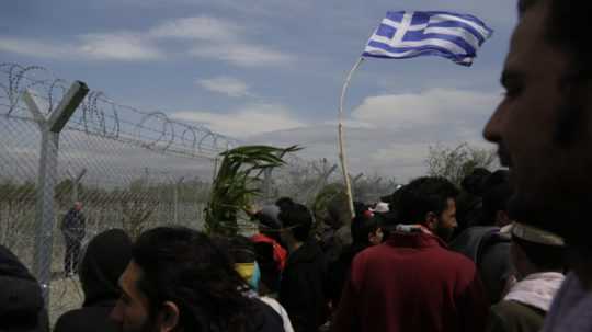 Migranti držia grécku zástavu pri plote