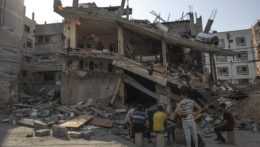 Na fotografii je skupina Palestínčanov a za nimi zničená budova, ktorú zasiahla izraelská raketa.