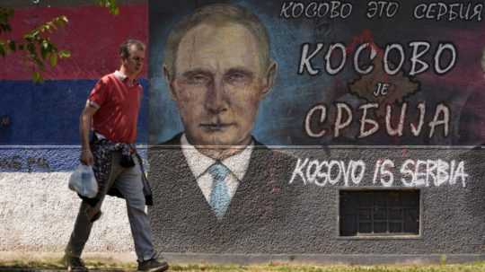 Muž prechádza okolo graffiti zobrazujúceho ruského prezidenta Vladimira Putina: "Kosovo je Srbsko".