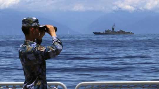Čínsky vojak sa cez ďalekohľad díva na taiwanskú vojnovú loď.