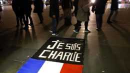 Ľudia prechádzajú okolo plagátu s nápisom „Je suis Charlie" počas zhromaždenia k prvému výročiu útoku na redakciu satirického časopisu Charlie Hebdo na Námestí republiky v Paríži.