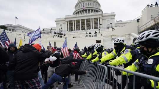 Stúpenci bývalého amerického prezidenta Donalda Trumpa sa snažia dostať cez bariéry pred budovou Kapitolu vo Washingtone v januári 2021.