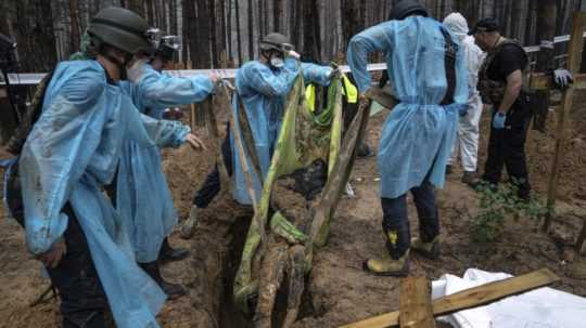 Príslušníci záchranných zložiek exhumujú telo civilistu v ukrajinskom meste Izium.