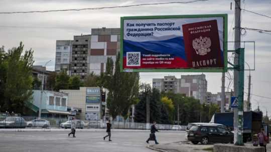 Ľudia kráčajú cez cestu okolo bilbordu s nápisom "Ako získať ruský pas? pred referendami o pripojení štyroch ukrajinských regiónov k Rusku v Luhansku na východe Ukrajiny.