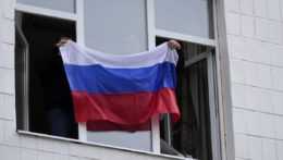 Muži držia ruskú vlajku z okna.