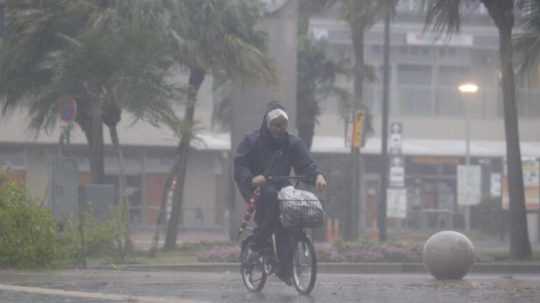 Na snímke muž na bicykli v uliciach Tokia bojuje s poryvmi vetra.