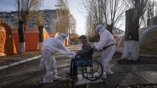 Lekári v špeciálnych ochranných odevoch privážajú staršieho pacienta na vozíku do poľnej nemocnice v meste Kachovka.