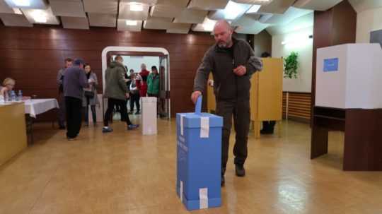 Volič hádže hlasovací lístok do modrej volebnej urny