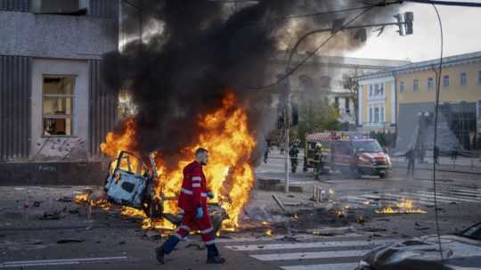Na snímke je zdravotník, ktorý uteká okolo horiaceho auta po ruskom raketovom útoku v Kyjeve