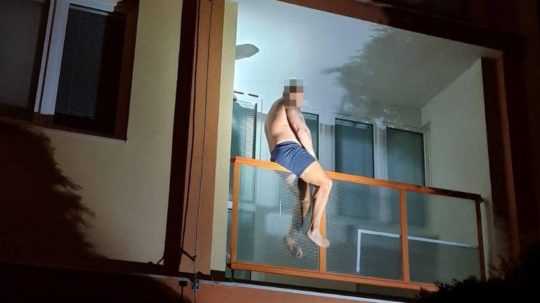 Na snímke je muž, ktorý lezie cez balkón.