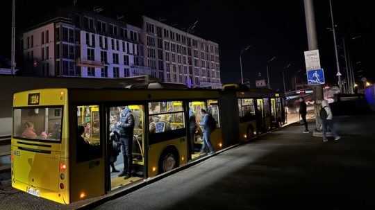 Ľudia nastupujú do autobusu na tmavej ulici v ukrajinskej metropole Kyjev.