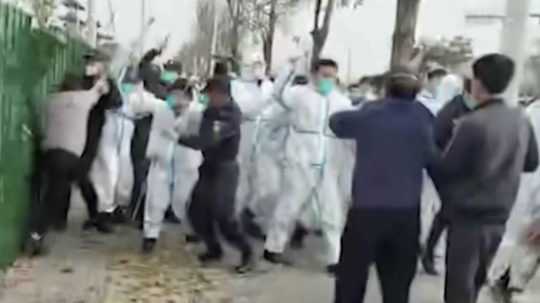 Na snímke bezpečnostný personál v ochrannom odeve zaútočil na muža počas protestu v areáli továrne spoločnosti Foxconn v čínskom meste Čeng-čou.