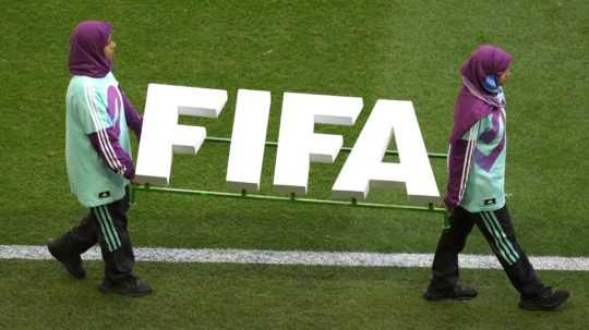 Príslušníčky upratovacej služby nesú na ihrisku nápis FIFA.