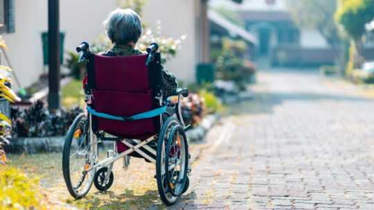 Na snímke žena v dôchodkovom veku sedí von pred domov invalidnom vozíku.