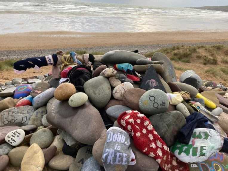 Na snímke je kôpka pomaľovaných kameňov a ponožiek na pláži.