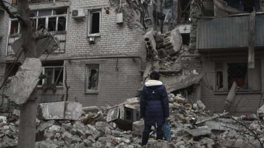 Žena sa pozerá na bytovku zničenú po nedávnom ruskom raketovom útoku v meste Časiv Jar v Doneckej oblasti na východe Ukrajiny
