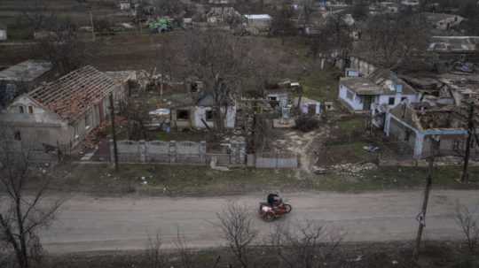 Na ilustračnej snímke muž jazdí na motorke pred zničenými domami po ruskom ostreľovaní.