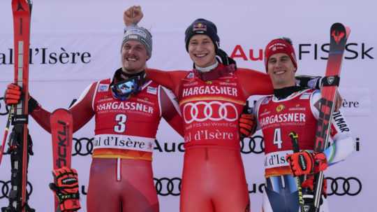 Švajčiarsky lyžiar Marco Odermatt (uprostred) oslavuje na pódiu s druhým Rakúšanom Manuelom Fellerom (vľavo) a tretím Slovincom Žanom Kranjecom (vpravo).