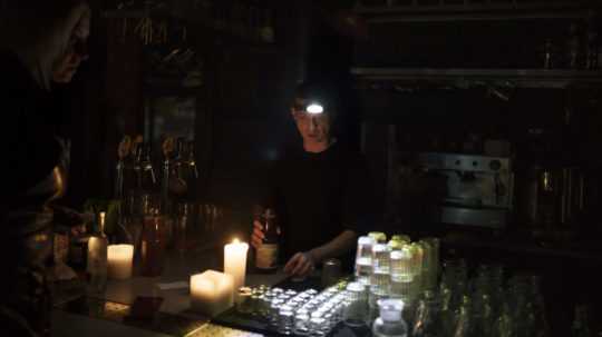 Barman pripravuje nápoj pomocou čelovej lampy počas výpadku elektriny v ukrajinskom hlavnom meste Kyjev.