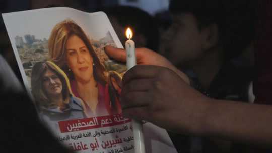 Palestínčan drží sviečku a fotografiu zavraždenej palestínsko-americkej novinárky Šírín abú Aklaovej v Gaze.
