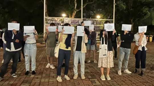 Na snímke držia ľudia pred svojimi tvárami listy papierov.