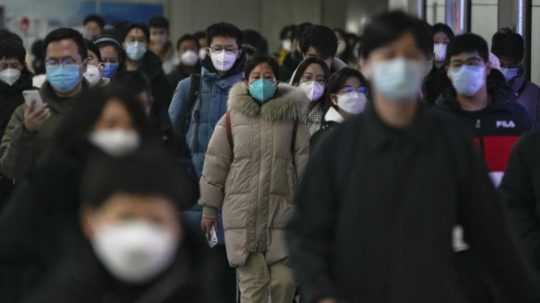 Cestujúci ochranných rúškach na stanici metra v Pekingu.