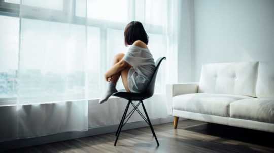 Na snímke je žena schúlená na stoličke a hľadí von oknom.
