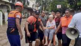 Záchranári prenášajú staršiu ženu počas záplav na Filipínach.