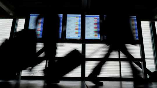 Na ilustračnej snímke cestujúci kráčajú okolo informačnej tabule na letisku.