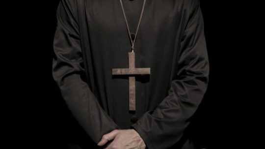 Na snímke je kňaz v čiernom habite a dreveným krížom na krku.