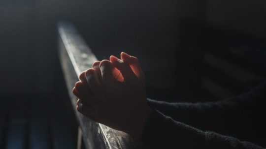 Na snímke je vidieť ruky modliacej sa osoby na stolci v kostole.