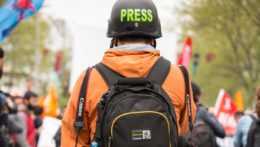 Na ilustračnej snímke stojí novinár na ulici s ochrannou helmou s napísom press (tlač)