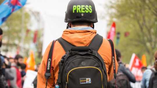 Na ilustračnej snímke stojí novinár na ulici s ochrannou helmou s napísom press (tlač)