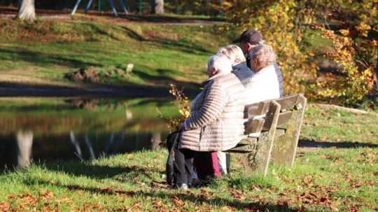 Dôchodkyne sedia na lavičke pri jazere.