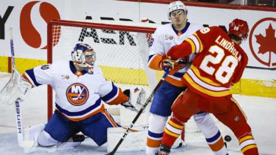 Na snímke ruský brankár Islanders Semjon Varlamov, jeho krajan a spoluhráč v obrane Alexander Romanov a švédsky útočník Calgary Elias Lindholm v zápase hokejovej NHL Calgary Flames - New York Islanders.