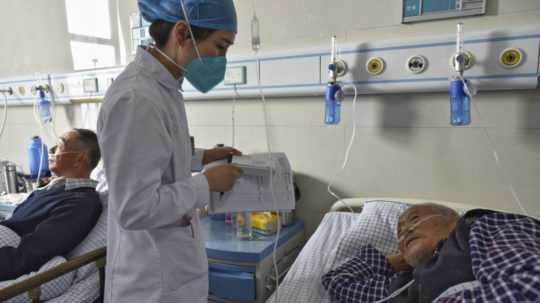 zdravotná sestra podáva lieky starším pacientom s príznakmi ochorenia COVID-19 v čínskej nemocnici.