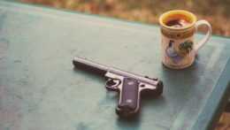 Na stole je položená pištoľ vedľa šálky s kávou.