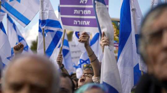 Izraelskí demonštranti mávajú národnými zástavami a transparentmi počas protestu.