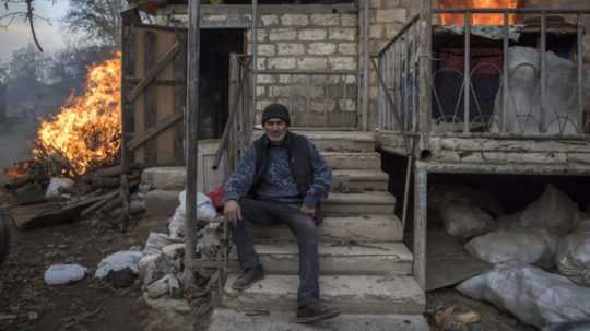Muž sediaci pred horiacim domom v dedine v Náhornom Karabachu.