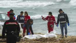 Dobrovoľníci talianskeho Červeného kríža a pobrežná stráž vyzdvihujú telo mŕtveho migranta.