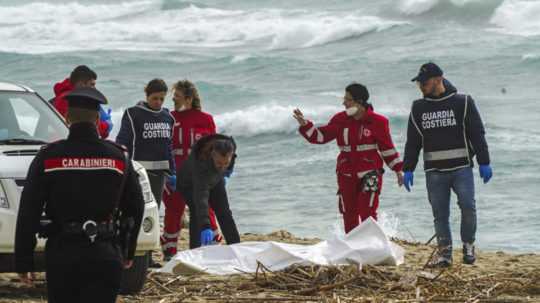 Dobrovoľníci talianskeho Červeného kríža a pobrežná stráž vyzdvihujú telo mŕtveho migranta.