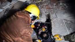 Záchranári vyťahujú ženu z trosiek zrútenej budovy.