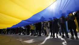 Ľudia držia obrovskú ukrajinskú vlajku počas zhromaždenia pri príležitosti ročného výročia ruskej invázie na Ukrajinu.