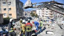Záchranári stoja na mieste zničenom zemetrasením, v pozadí bager.
