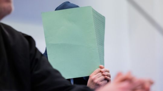 Na snímke si odsúdený muž zakrýva tvár zeleným dokumentom.